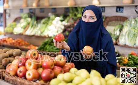 Delighted young Muslim woman purchaser choosing apples in grocery store