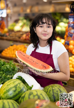 Positive girl seller of grocery supermarket with ripe watermelon in her hands