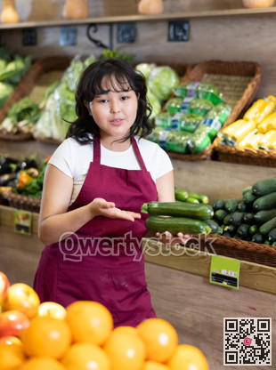 Smiling young saleswoman holding cucumbers in grocery store