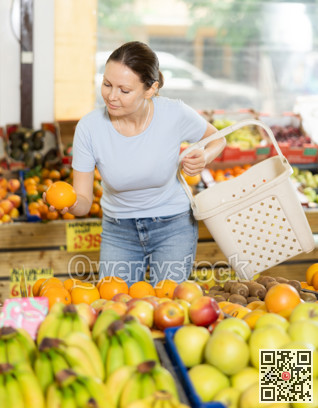Delighted woman purchaser choosing oranges at the counter in grocery store