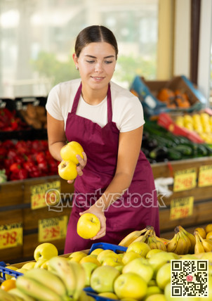 Girl seller of garden-stuff store works near showcase, sorting apples, checking goods