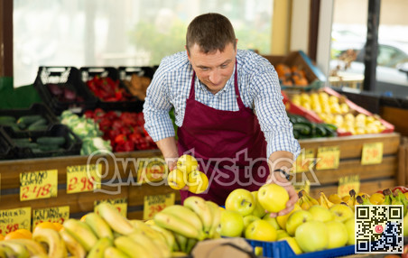 Man seller working in supermarket and lays out apples on counter