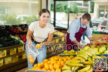 Young female shopper selects and buys fresh oranges in supermarket