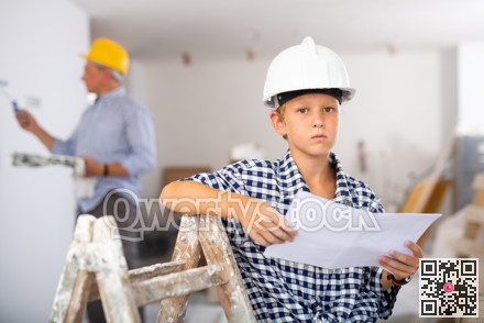 Portrait of young boy in hardhat with documents in building site