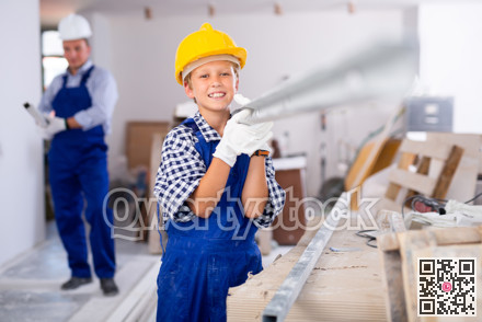 Boy carrying metal plank with his father in construction site