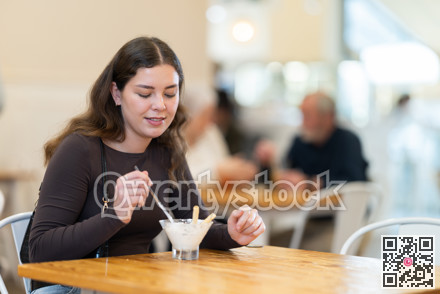 Girl happily eats delicious ice cream while sitting at a table in cafe