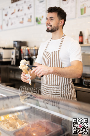 Positive man in an apron offers ice cream at dessert counter with an inviting smile