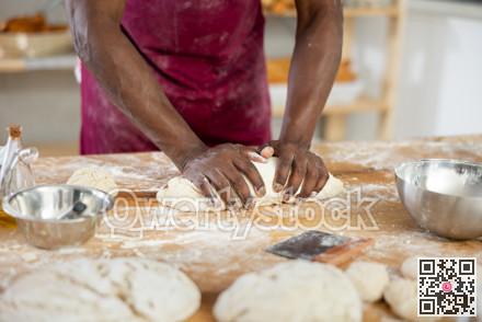 Hands of African baker kneading dough on floury table