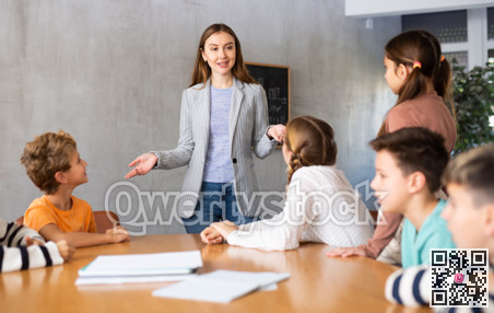 Inspired young female teacher working with preteens schoolgirls and schoolboys in modern classroom