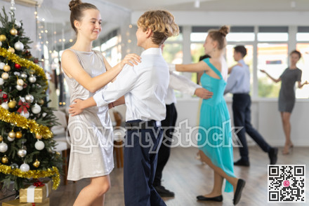 Teen boy and girl dancing waltz in couple during lesson at studio in New Year atmosphere