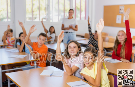 Group of school pupils raise their hands up in classroom during lesson in school