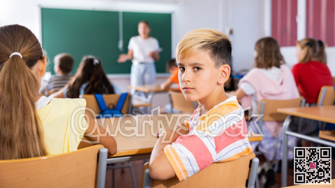 Schoolboy sits half-turned at desk in classroom at lesson in elementary school