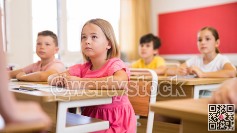 Focused small schoolgirl writing in workbook during lesson in class