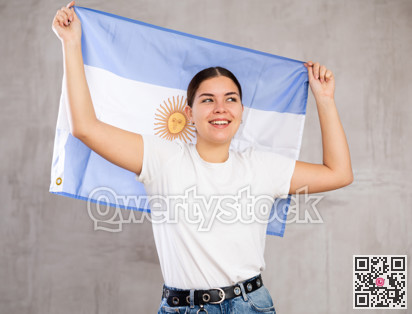 Excited young woman holding state flag of Argentina against gray wall background indoors