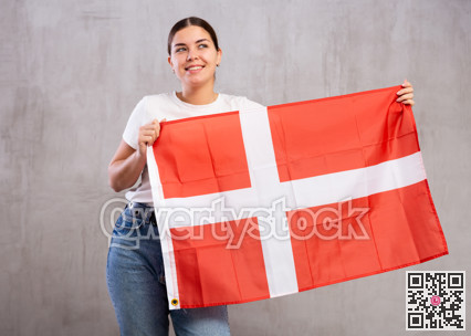 Joyous young woman holding Denmark flag against unicoloured background