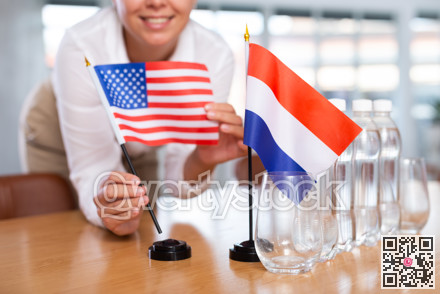 Young woman puts USA and Netherlands flags on table in office