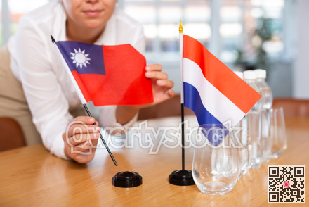 Woman secretary prepares an office for negotiations - she places flags of Taiwan and Netherlands table