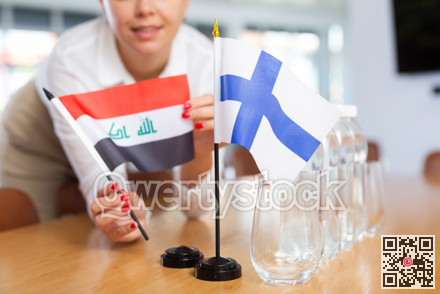 Female secretary places flags of the Iraq and Finland flag on the table before negotiations of top political figures