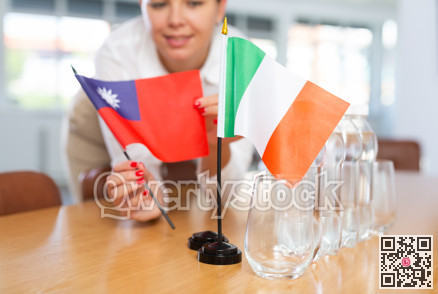 Young woman putting Taiwan and Italy flags on table in office