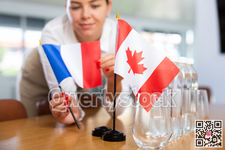 Young woman puts flags of France and Canada on table in office