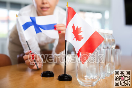 Young woman putting flags of Finland and Canada on table in office