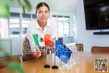Female secretary places flags of the European Union and Mexico flag on the table before negotiations of top political figures