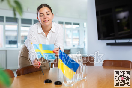 Businesswoman setting flags of Ukraine and Sweden on negotiating table