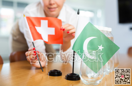 Little flag of Pakistan on table and flag of Switzerland put next to it by young woman