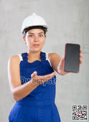 Young woman in work overalls posing with phone