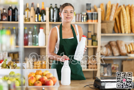 Young woman seller offering milk in grocery store