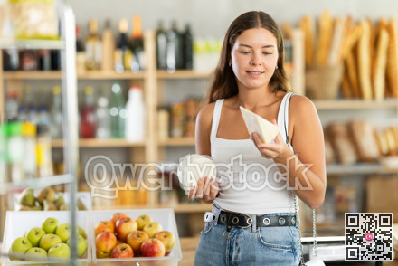 Young girl carefully chooses delicious cheese in grocery department of supermarket