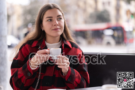 Girl in plaid jacket sits at table in street cafe, drink tea