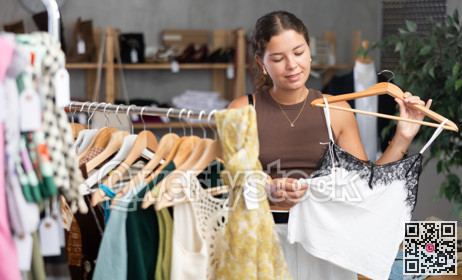 Girl customer choose crop top in store, and buyer carefully examines product.