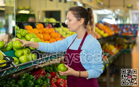 Middle-aged saleswoman putting apples on food stall in grocery store