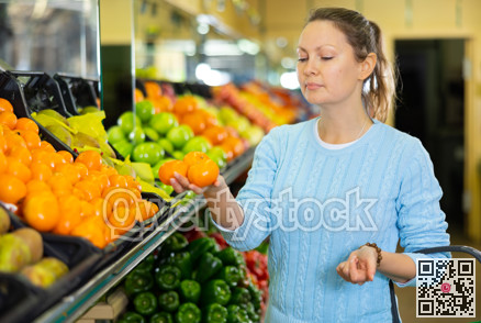 Positive middle-aged female buyer in casual wear choosing tangerines fruits in grocery store