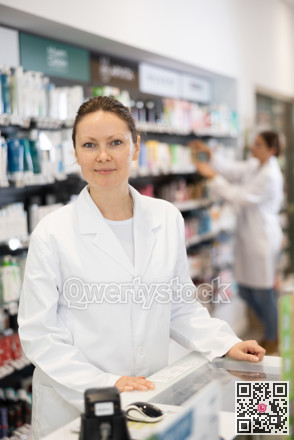 Adult female pharmacist posing at cash register in pharmacy