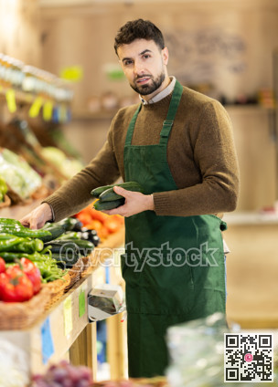 Young man seller puts cucumbers in store