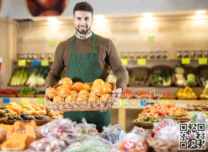 Young man seller puts oranges in vegetable shop