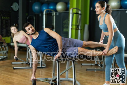 Female trainer helping young man performing side plank on pilates chair