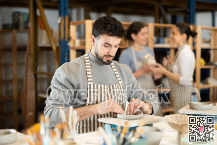 Guy sitting at table, busy making products from raw clay