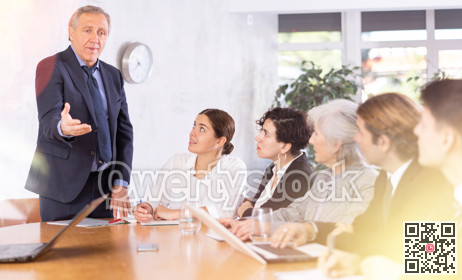 Annoyed senior male boss yelling at office colleagues of different ages taking notes at table with laptops