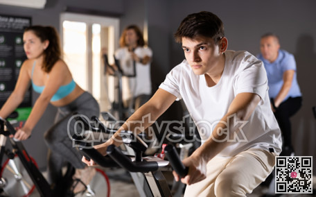 People in activewear warming up on training using exercise bike in gym