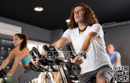 Sporty man working out on stationary bicycle in gym