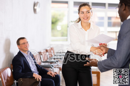Woman makes deal, shaking hands with middle-aged African man colleague while standing in office