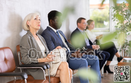 Serious-minded mature female candidate siting on chair and waiting for job interview in hallway