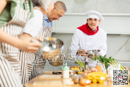 Positive young man chef of cooking course teaching attendees how to mix sauce