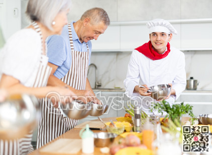 Positive young man chef of cooking course teaching attendees how to mix sauce