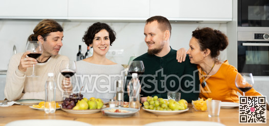 Two married couples are sitting at table, enjoying food and wine, chatting, talking, laughing.