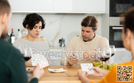 Happy group of friends playing poker cards and drinking wine