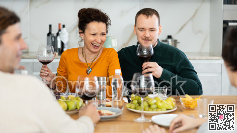 Group of happy celebrating holiday drinking and chatting at table at kitchen